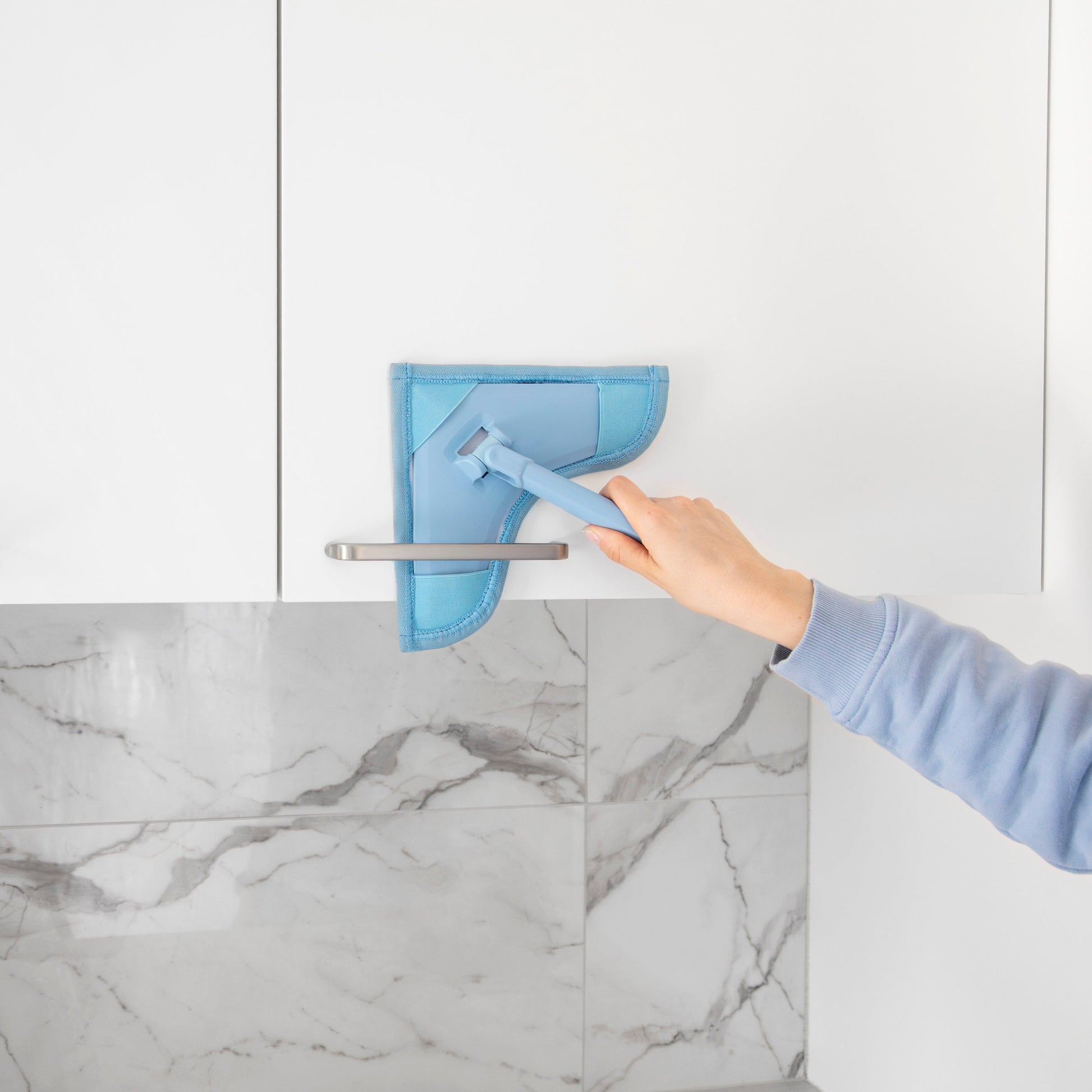 Person cleaning a marble countertop with a blue cleaning tool.