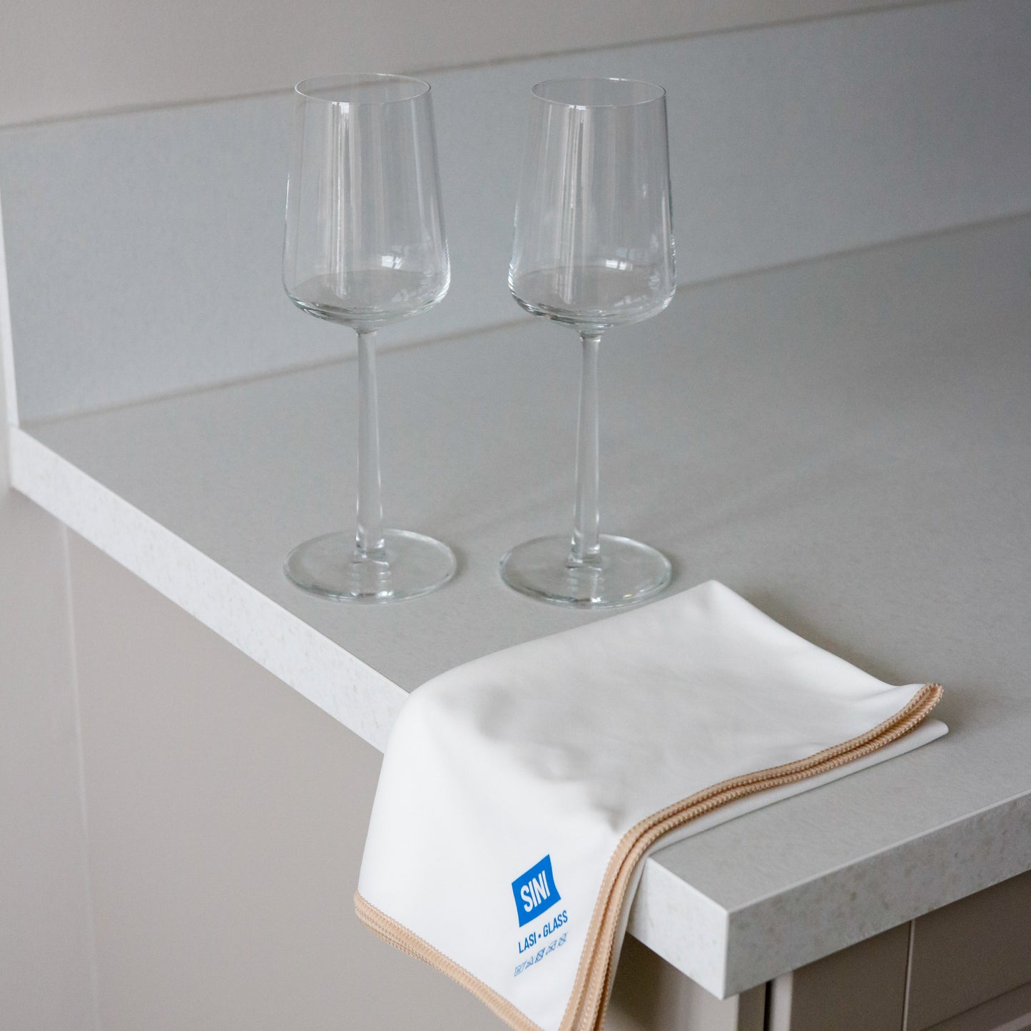 Two wine glasses on a countertop with a towel featuring a logo.