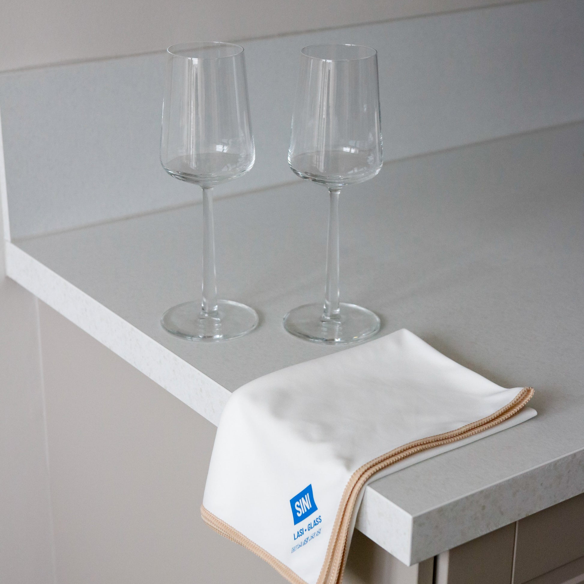 Two wine glasses on a countertop with a towel featuring a logo.