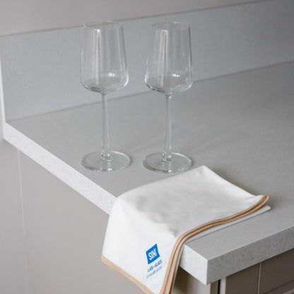 Two wine glasses on a countertop with a towel featuring a logo.