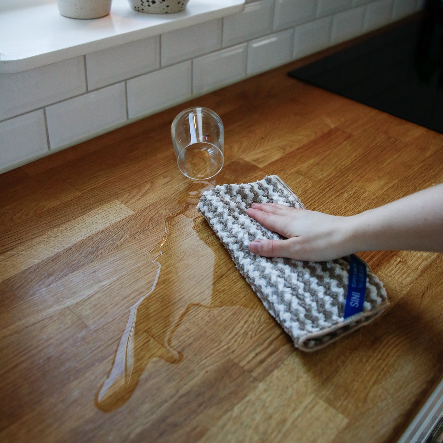 Person cleaning a spill on a wooden surface with a cloth.